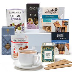 Assorted items in a luxury snack hamper, including tea, shortbread, flatbread, cheese bites, olives, peanuts, and popcorn