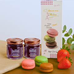 Two jars of Mrs. Bridges Raspberry Preserve with pink, green, and brown macarons arranged beside them on a linen cloth for a luxurious afternoon tea